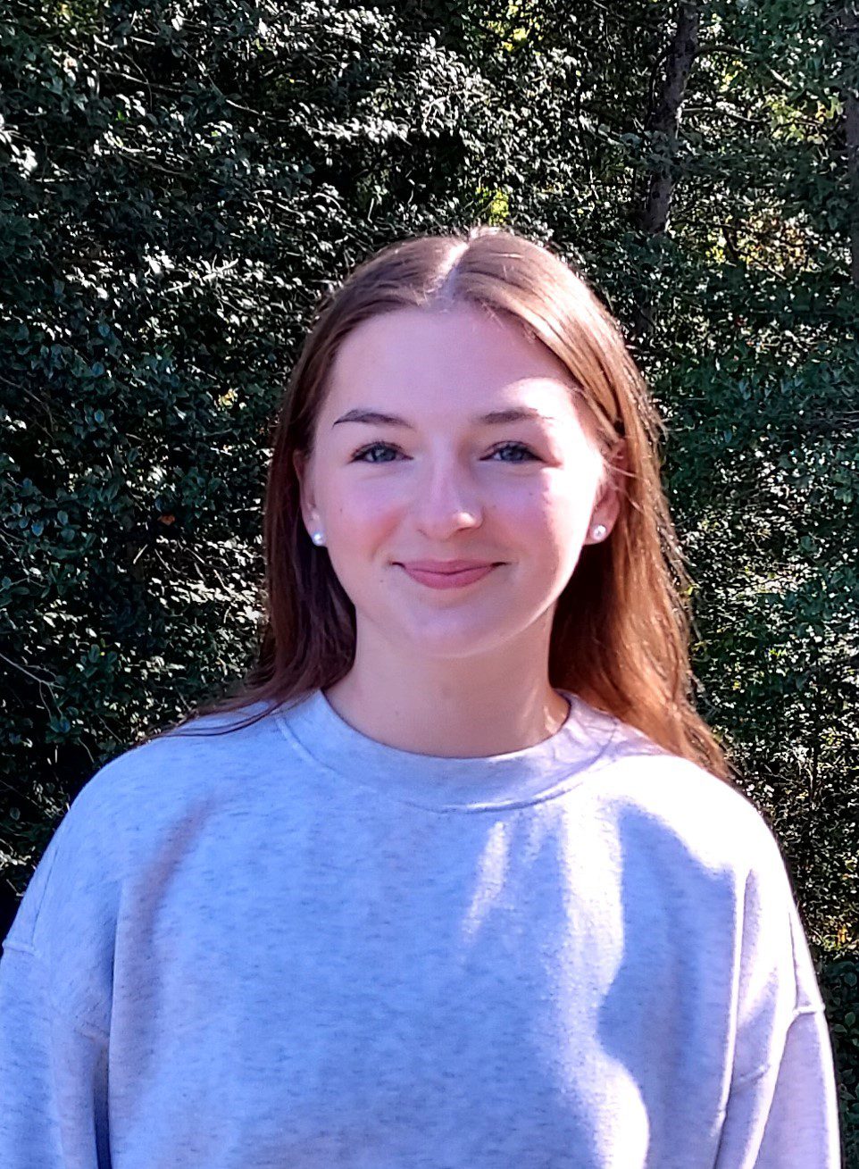 Smiling young woman outdoors against leafy background
